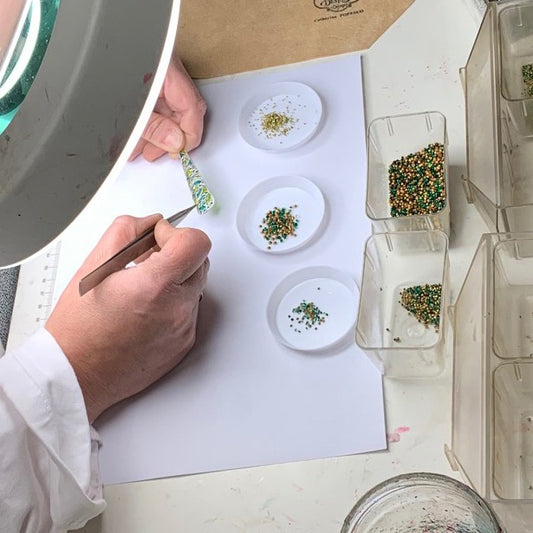 Gros plan sur les mains d'un artisan en train de réparer des boucles d'oreilles via le collage de strass